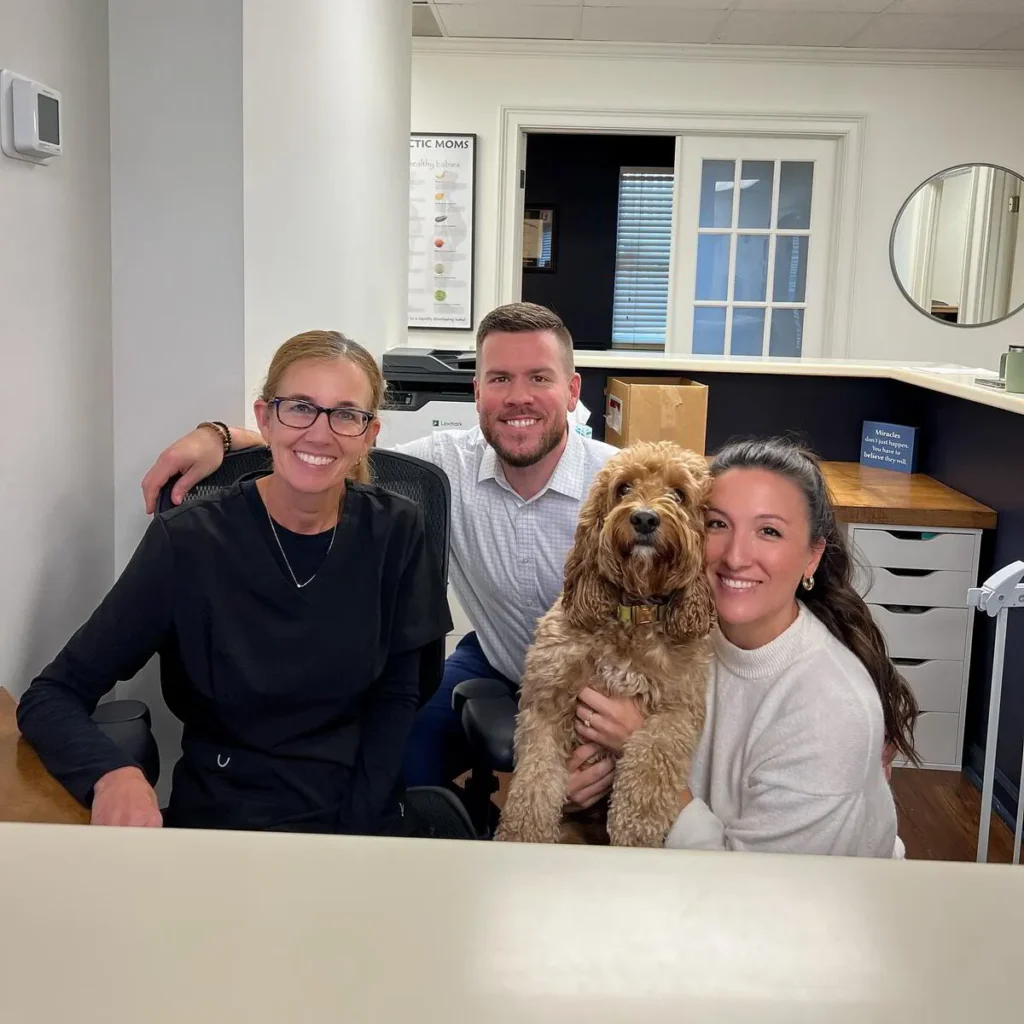 Animal chiropractic staff smiling with a fluffy dog at the front desk of a welcoming clinic
