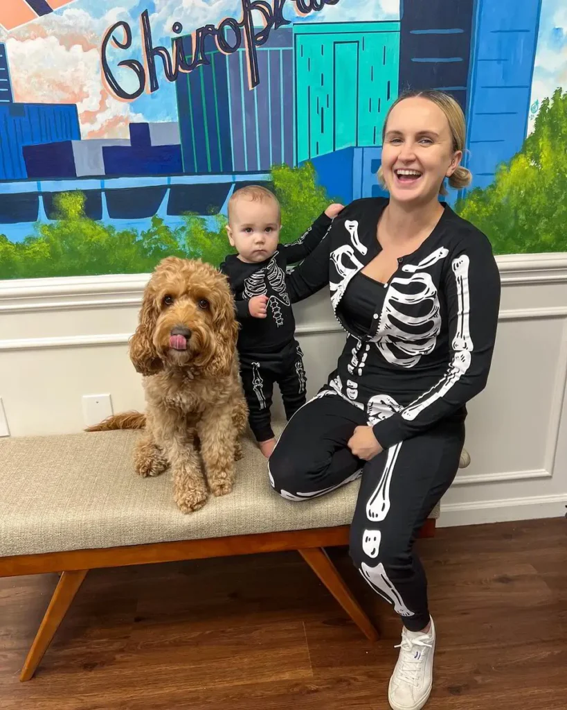 Smiling parent and baby sitting beside a curly coated dog inside a colorful animal wellness space