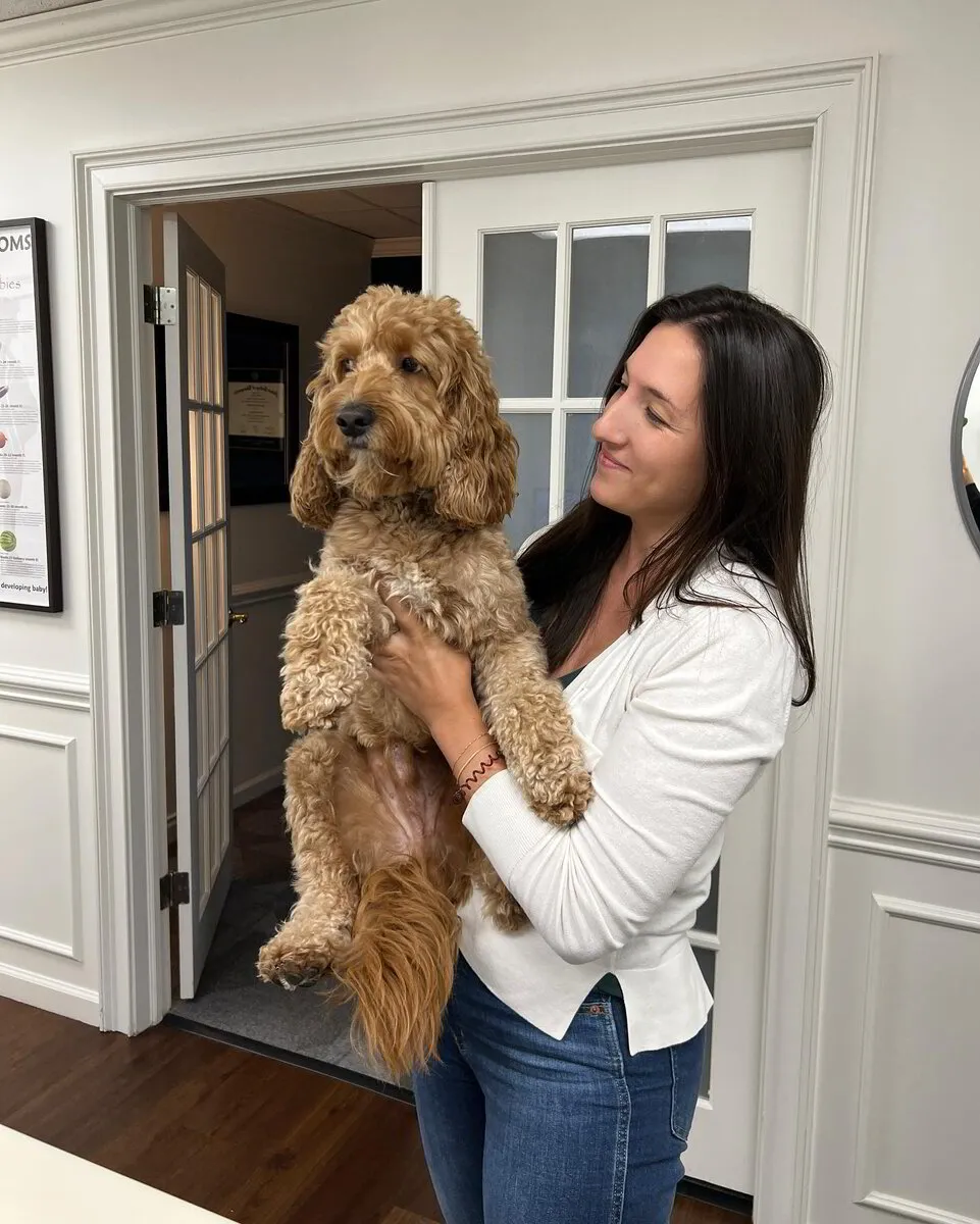 Dr. Megan holding a curly haired dog inside a bright reception area
